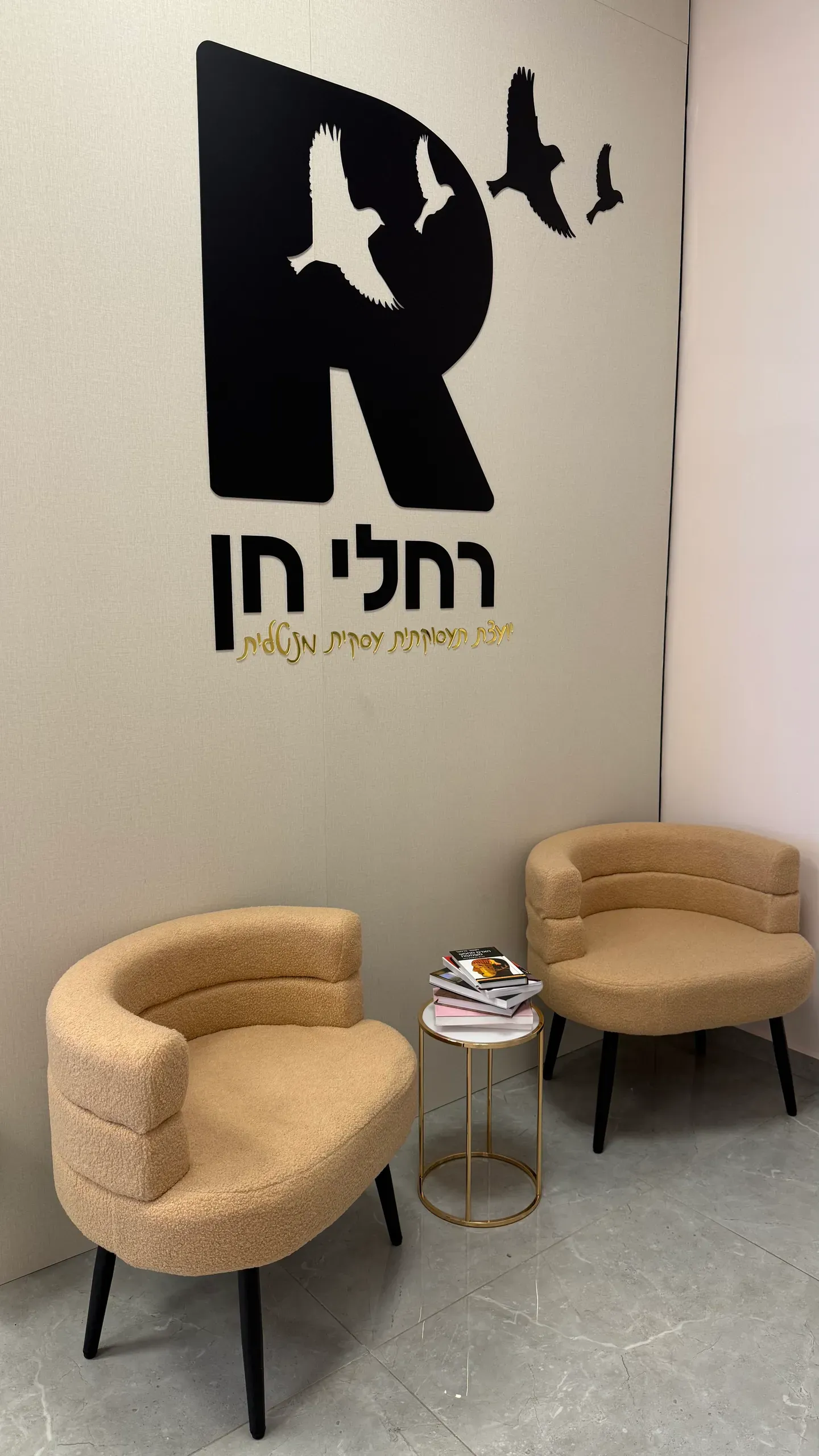 פינת ההמתנה במרכז, שני כורסאות בהירות מתחת ללוגו על הקיר